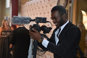 male student in suit holding camera and smiling