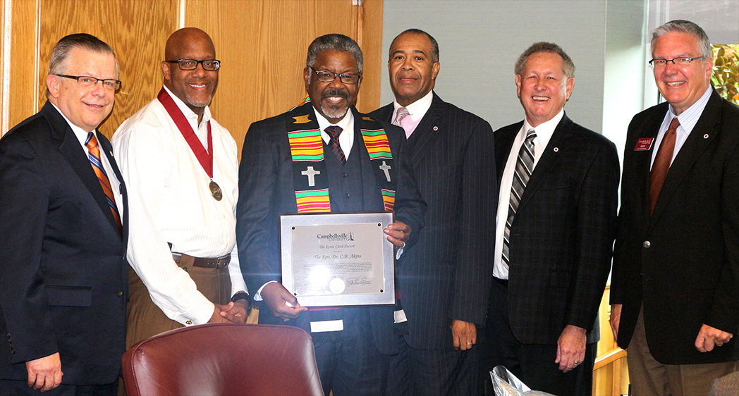 five men around another man holding award